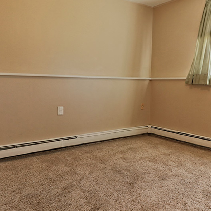 Room with beige walls, carpet flooring, and a baseboard heater.