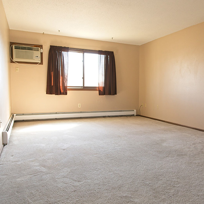 Room with beige walls, carpet flooring, a window with dark curtains, and a wall-mounted AC unit.